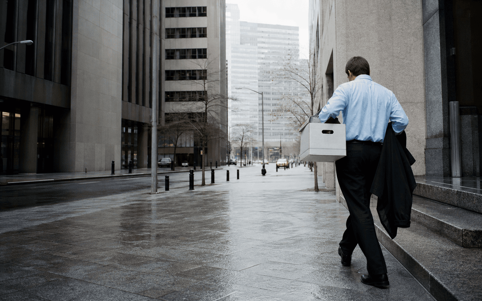Un lavoratore della finanza porta una scatola fuori da un edificio durante una giornata grigia a Manhattan